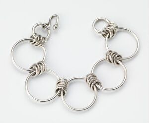  "Ringer" by Tone Vigeland, a piece of silver jewelry composed of interconnected silver rings of varying sizes, with smaller rings featuring tightly coiled wire, all crafted using combined rings of silver and forging techniques.