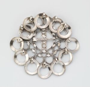  An intricately designed silver metalwork ornament with a symmetrical pattern of circular motifs and a central cross-like embellishment, set against a light gray background.