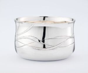  A reflective silver bowl with decorative, wavy lines etched around its exterior, sitting against a solid light gray background.