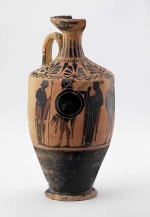  An ancient Greek amphora from the Phanyllis-gruppe collection, featuring beige and black colors with black-figure painting. The vessel has two vertical handles and a detailed scene with human figures on its main body.