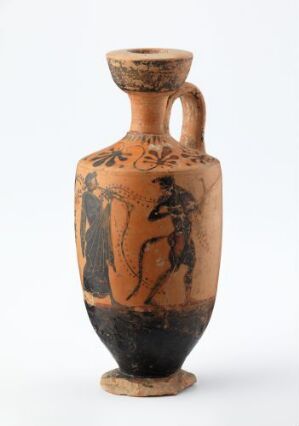  An ancient Greek black-figure amphora, featuring two stylized figures, one standing with a staff and the other in motion possibly dancing, against a reddish-tan background with glossy black on top and bottom, displayed against a neutral off-white background.