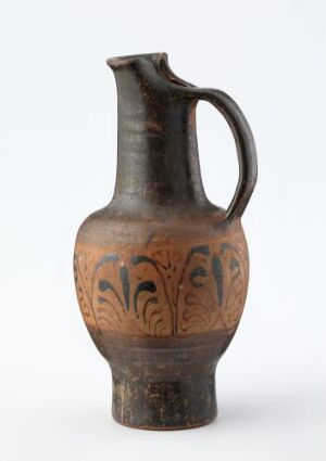  A ceramic jug with a bulbous body and long neck featuring a decorative band of leaf-like motifs around the center, set against a light-grey background. The jug's colors range from deep brown to black at the neck and handle, with lighter brown hues on the body.