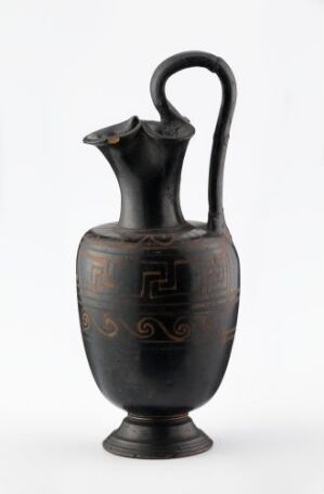  An ancient-style dark ceramic vase with a single handle and incised decoration, on a light background. Artist name and title are unknown.