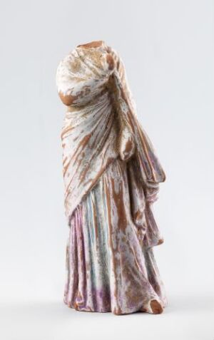  A photograph of a sculptural figure entirely covered by a draped, multicolored cloth in shades of off-white, beige, lavender, pink, and soft blues, standing against a plain light background.