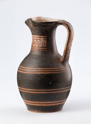  An ancient terracotta jug with a bulbous body, narrow neck, and a single handle. The jug displays horizontal tan and brown bands with a decorative pattern around its midsection against a neutral grey background.