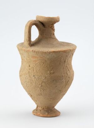  A sandy beige, textured pottery jug with a single handle, conical body, narrow neck, and rounded lip, likely from an ancient or handcrafted origin.