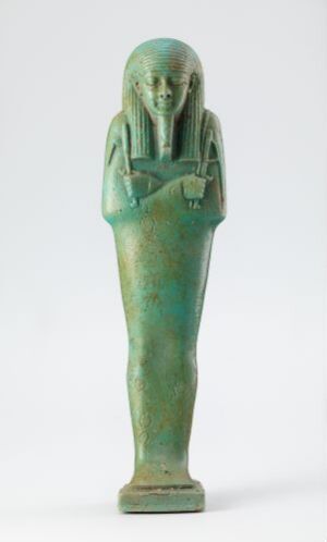  An ancient Egyptian turquoise faience statuette from the grave of Hekaemsaf, overseer of the royal ships, depicting a slender, elongated figure standing upright with crossed hands, in the style of a high-status individual from ancient Egypt. The figure has stylized facial features and wears a simple, pleated garment. The material's vibrant turquoise color shows variations in tone due to age. The artist's name is unidentified.