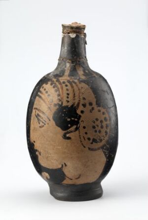  An ancient ceramic flask with a narrow neck and bulbous base, featuring a black-figure profile of a human face with tan decorative patterns on a black background, against a light grey backdrop.