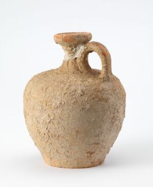  A globular beige terracotta jug with a single sturdy handle, having a rough-textured surface with slight color variations, displayed against a light-colored background. Artist name and title unknown.