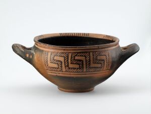  An ancient terracotta bowl with a dark interior and a geometric key pattern below the rim. The bowl has two curved handles and exhibits a gradient from deep terracotta to a lighter sandy color.