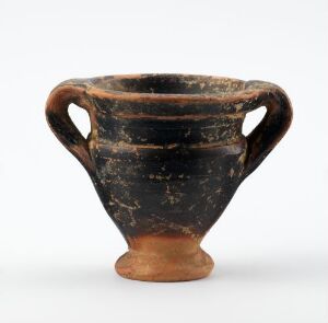  An ancient ceramic vase with two handles, predominantly black with natural tan clay highlights revealing its historical texture and wear.