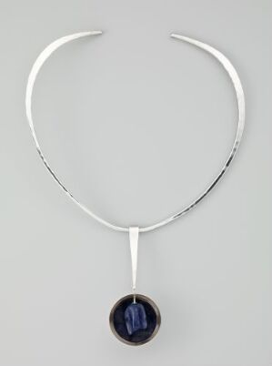  Silver necklace designed by Erling Christoffersen, titled "H 57", featuring a minimalist silver band with a blue gemstone pendant against a neutral background.