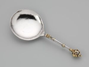  An antique forged and cast silver spoon with gilded details and intricately designed handle known as "Sølvskje" by an unidentified artist, against a neutral gray background. The decorative spoon is associated with the serving and consumption of food, showcasing a polished silver bowl and ornate handle with gold accents.