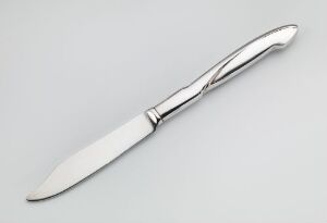  A silver table knife with a decorative handle lies on a plain gray background, showcasing a polished metallic finish and an elegant, sculpted design.