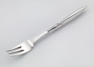  A silver metal fork with four tines and a slender handle lies on a light gray background, reflecting light on its glossy surface.