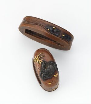  Two traditional Japanese netsuke carvings resembling stylized shoes, one open and flat with a central ridge, decorated with black and gold patterns, and the other featuring a detailed lobster sculpture with deep brown and golden hues, both exhibiting a polished finish.