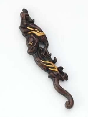  A detailed wooden carving of a lizard with golden streaks along its back on an off-white background.