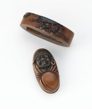  Two small, brown, intricately carved objects on an off-white background; one is a narrow, oblong container with a classical scene in relief, and the other is an oval-shaped portrait in high relief of a man's face with classical features.