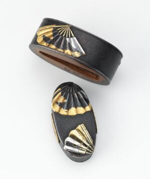  A set of two matching pieces of jewelry, a wide black cuff bracelet and an oval-shaped ring, both adorned with reflective gold and cream fan-like patterns against a black background.