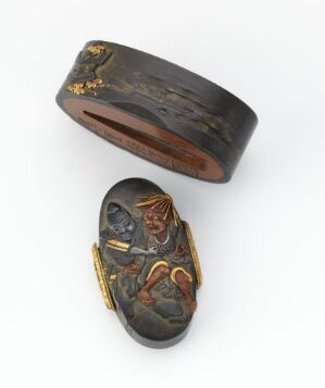  Two antique oval-shaped rings with flat bezels, one lying sideways with a wide band featuring golden inlay and patterns, and the other with its bezel upwards showing a classical figure carved in intaglio with golden accents, against a white background.