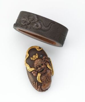 
 Two antique objects: on the left, a dark brown bracelet with a floral pattern, and on the right, an oval-shaped dark brown brooch or cameo with a gold-highlighted figure resembling a mythical creature or small cherub.