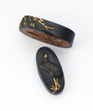  Two oval-shaped black and gold decorative objects, possibly jewelry, on a white background; one is an elongated flat piece with a golden bird in mid-flight, and the other is a broad band with abstract golden patterns. Artistname and title are unknown.