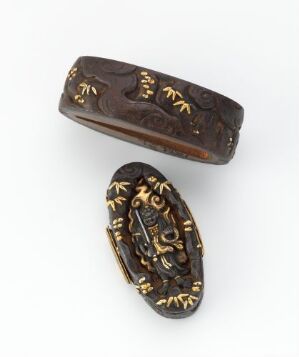  Two oval-shaped, dark brown artifacts with gold-colored inlay patterns, lying against a light background, possibly ancient bracelets or bangles.