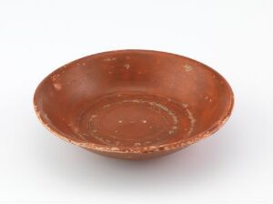  An ancient-style terracotta bowl with a worn surface and circular ridged patterns inside, displayed against a light background.