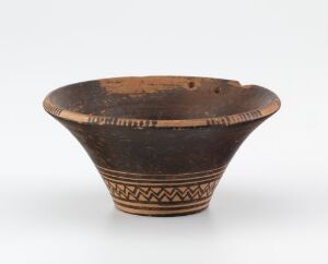  An ancient pottery bowl with a wide, flared opening and a tapered base, featuring dark and light brown colors with decorative patterns etched near the rim and base.