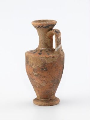  An ancient, earthy brown pottery jug with a narrow base, rounded body, and a single thick handle. The jug has a textured and weathered appearance, indicative of considerable age, set against a light-grey background.