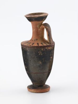  An ancient brown and black mottled pottery vessel with a curved body, a single handle, and a flared mouth, displayed against a plain light background.