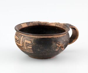  A handcrafted terracotta cup known as "barnekopp," with intricate tan geometric patterns on a dark brown background, created by an unknown artist. The cup has a smooth, rounded body with a single handle, demonstrating traditional turning and modeling techniques in its design.