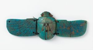  An ancient Egyptian faience scarab with detailed carvings, predominantly bluish-green in color, designed to be sewn onto mummy wrappings. The object has spread wings with inscribed lines and symmetrical shapes, conveying a religious significance in the context of Egyptian burial practices.