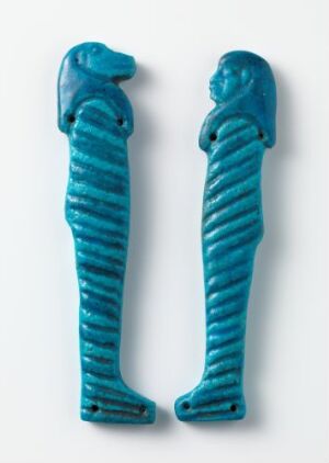  Two ancient Egyptian turquoise amulets representing the gods Hapi and Imsety. The amulets depict stylized human figures in a traditional Egyptian fashion, with prominent headdress and mummiform bodies, both exhibiting a textured and vibrant turquoise color. They are presented against a plain background, highlighting their cultural and historical significance.