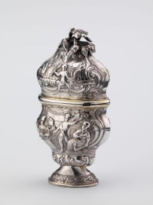  An ornate silver urn with embossed mythological figures, tapering to a narrow base and topped with a detailed matching lid, standing against a neutral background. Artist name and title are unknown.