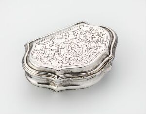  A silver-colored, shell-shaped metal object with intricate, etched floral patterns on the top surface, situated against a plain background.