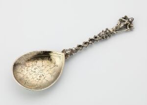  A silver spoon titled "Skje" by an unidentified artist, featuring a gilded, engraved bowl with floral motifs and a decorative handle with three-dimensional shapes, showcasing a metallic sheen and artisanal craftsmanship.