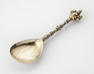  An ornate gilded silver spoon with a broad, oval-shaped bowl and a highly detailed handle culminating in a decorative flourish at the end, created by an unidentified artist. The spoon, titled "Skje," is indicative of skilled silverwork with forged and chased detail.