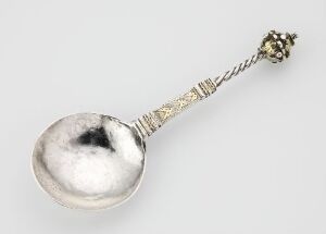  A silver spoon known as "Skje" by artist Jost Albertszenn featuring a reflective bowl and an ornately engraved handle with gilded detailing, exemplifying classic design and silver-smithing techniques.