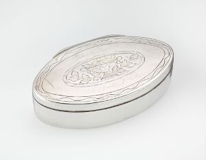  An oval-shaped metallic container with an intricately engraved lid, exhibiting a polished silver-like finish on a plain light gray background.