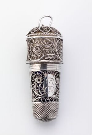  An ornate cylindrical silver object with a domed, patterned lid and an intricately designed body featuring filigree, a central embossed figure, and geometrical lattice-like patterns. The object is a stunning example of metal craftsmanship with varying hues of silver.