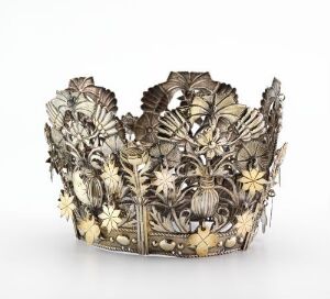  A traditional "Brudekrone," or bridal crown, made from gilded and engraved silver with pierced and stamped botanical motifs, created by an unidentified artist. The crown features a complex design of flowers and leaves in silver with accents of gold, showcased against a neutral background.