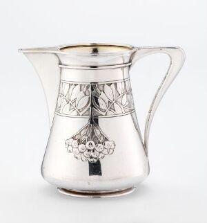  Silver cream jug titled "Fløtemugge" by Gustav Gaudernack, displaying a hammered and chiseled design with decorative openwork and embossed berry-like clusters on the body, a wide handle, and an elegantly flared pouring spout.