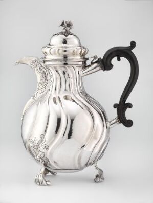  An antique silver pitcher with a sculpted, bulbous body and reflective surface, accented by a contrasting dark handle and an ornate, hinged lid with a decorative finial.