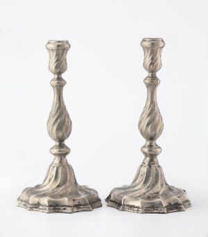  A pair of silver candlestick holders with a twisted stem design set against a light-gray background, displaying an antique elegance.