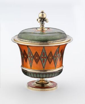  An ornate decorative container with a vibrant orange middle section adorned with dark diamond patterns, a muted green dome-shaped lid, golden finial, and base - suggesting a luxurious and historical artifact.