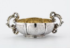  Antique silver drinking vessel, titled "Drikkebeger," by an unidentified artist, featuring a textured outer surface divided into panels and two ornate handles, with the interior gilded in gold.