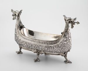  An intricately designed silver boat-shaped container with ornate animal paw legs and mythical creature heads at the ends, featuring detailed floral patterns along the exterior.