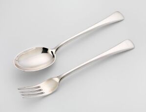  Two pieces of cast silver tableware consisting of a spoon and a fork with a polished finish, lying on a light gray background. The utensils feature a simple, elegant design and are crafted by artist Jacob Tostrup Prytz. The title of the artwork is unknown.