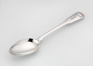  A polished metal spoon with ornate engravings on the handle, resting on a light grey surface.